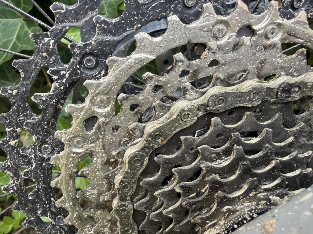 Mud-caked Shimano XT 12-speed cassette with a Shimano CN-M6100 chain on a large cog, sand packed into the gaps between the cogs