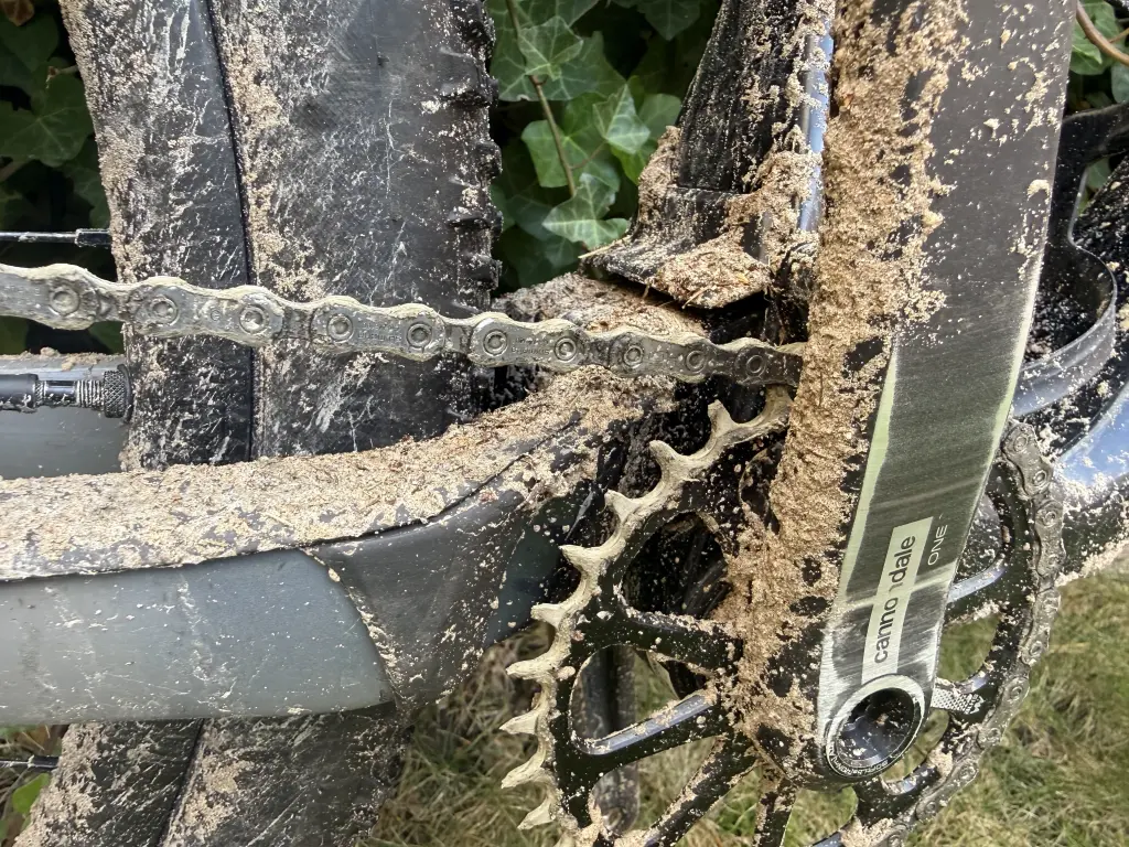 Shimano 12-speed chain coated in a sandy mud film running over a muddy Cannondale chainstay