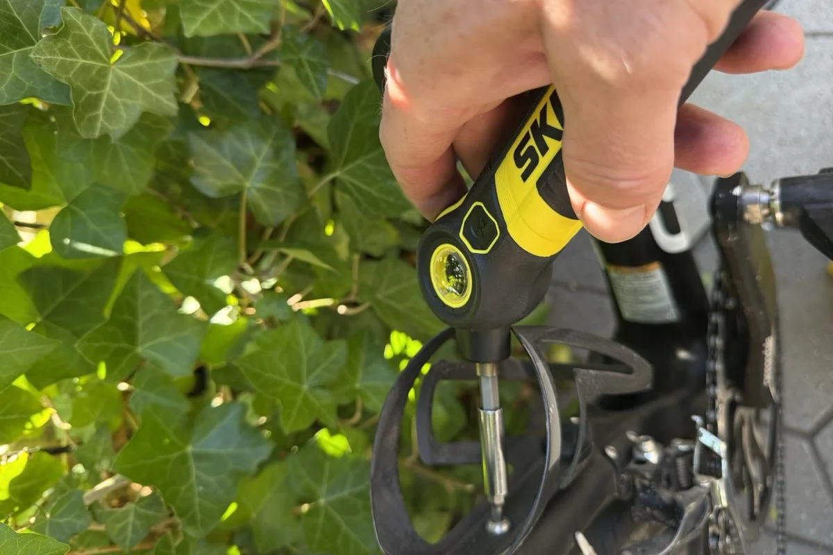 The screwdriver's head pivoted to 45 degrees with a long bit reaching a bottle cage bolt with the cage still fitted to the frame