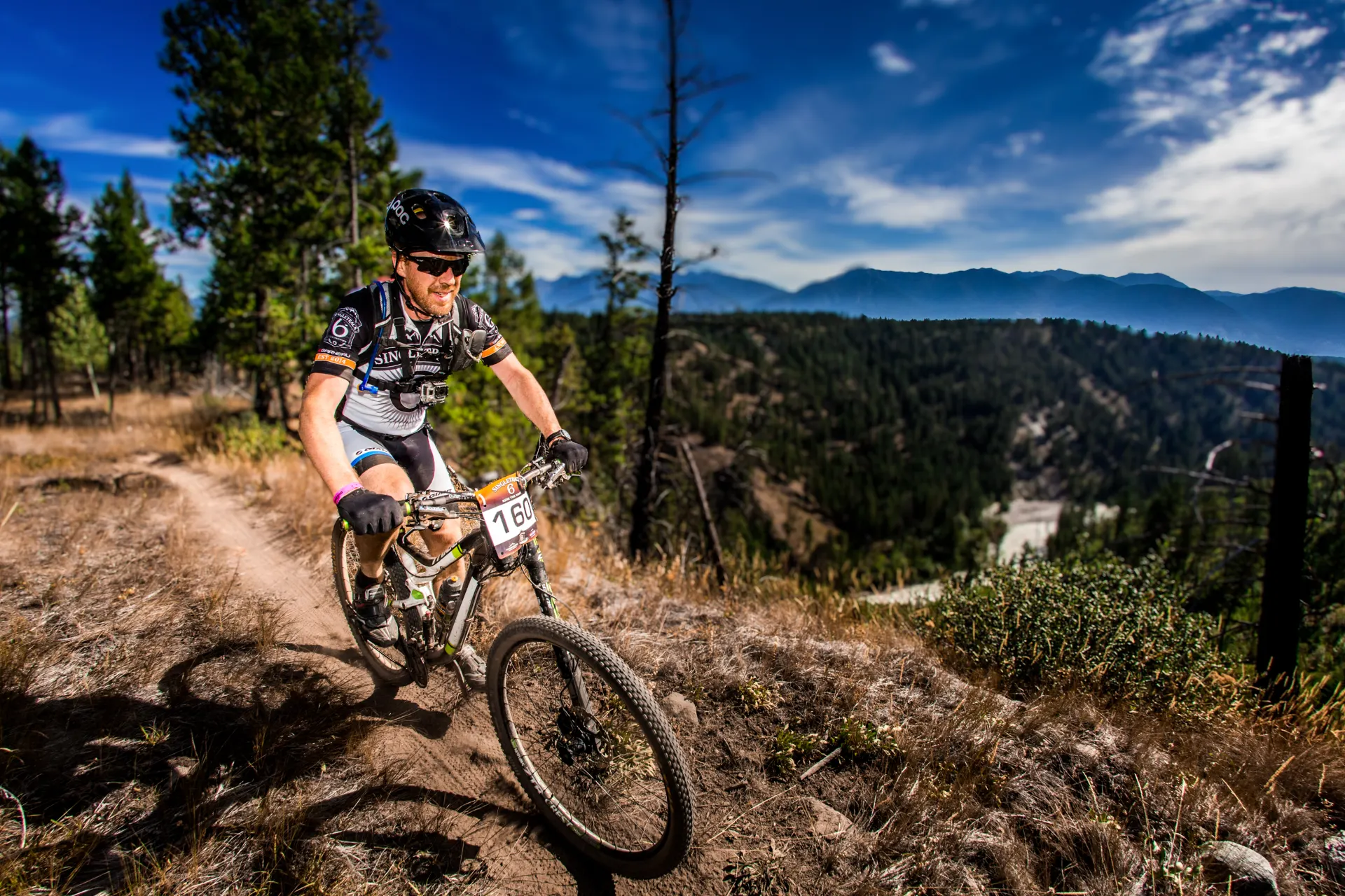Zwei Mountainbiker auf einem Gipfel mit Blick über bewaldete Berge.